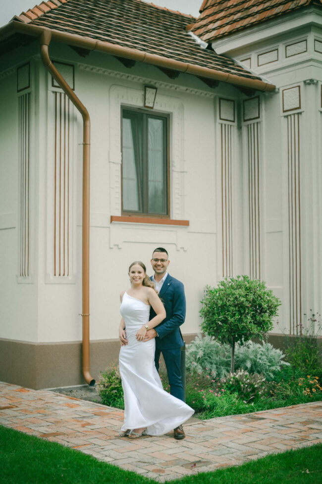 Elegáns esküvői kreatív fotózás, a menyasszony és a vőlegény egy klasszikus épület sétányán áll.