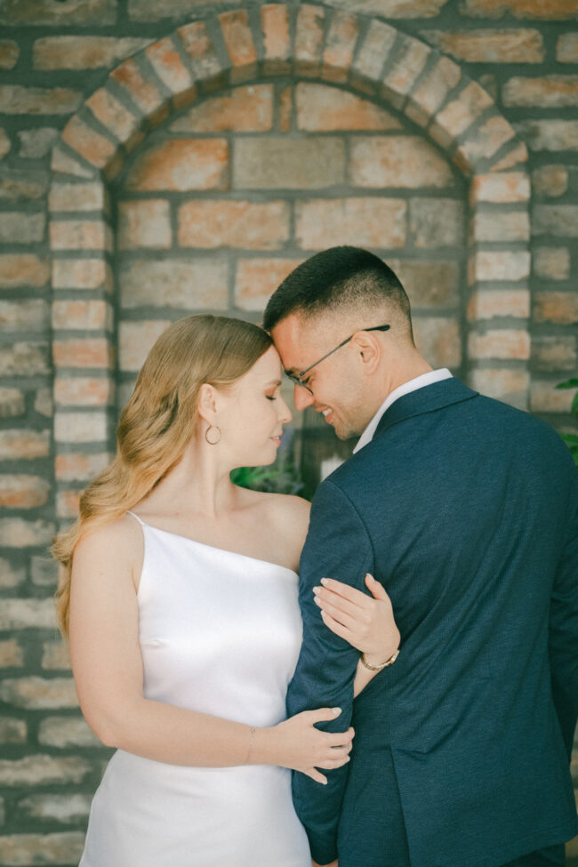 Intim, romantikus esküvői portré, a pár homlokukat egymásnak vetve áll egy téglaív alatt.