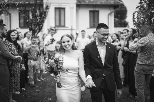 Felszabadult, fekete-fehér pillanatkép a polgári esküvő utáni kivonulásról, ahogy a násznép ünnepli a párt.